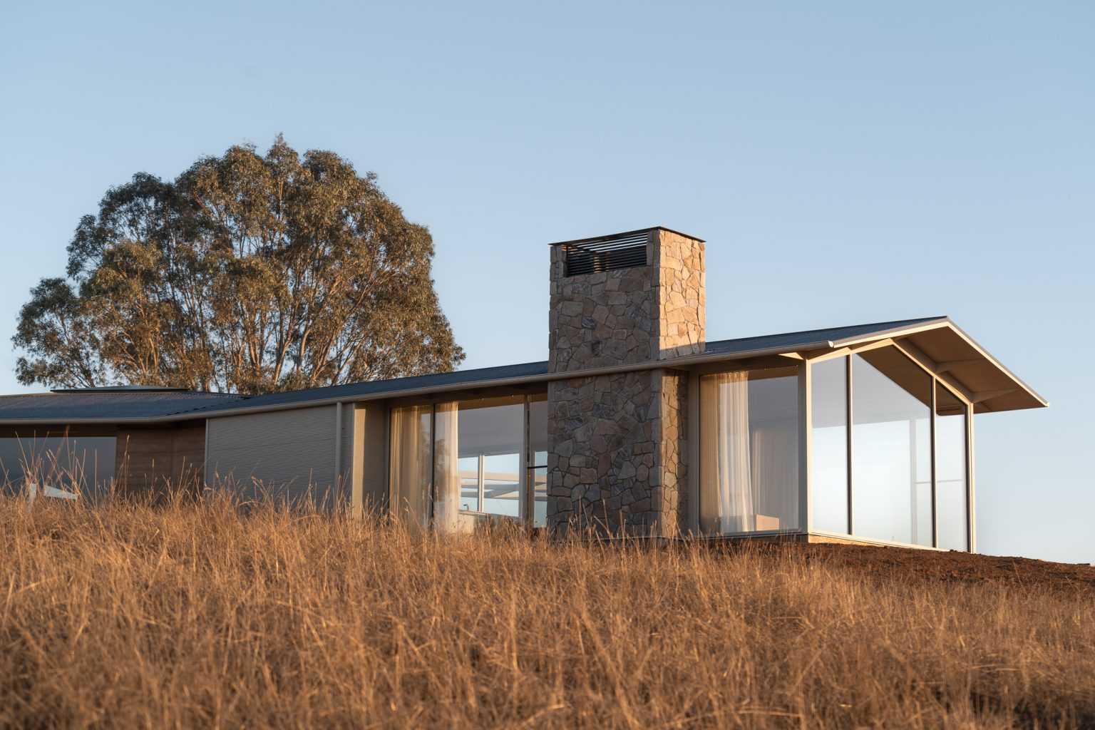 A frame of an external view of Table Top House with large fixed pane windows that provide views over Lake Hume.