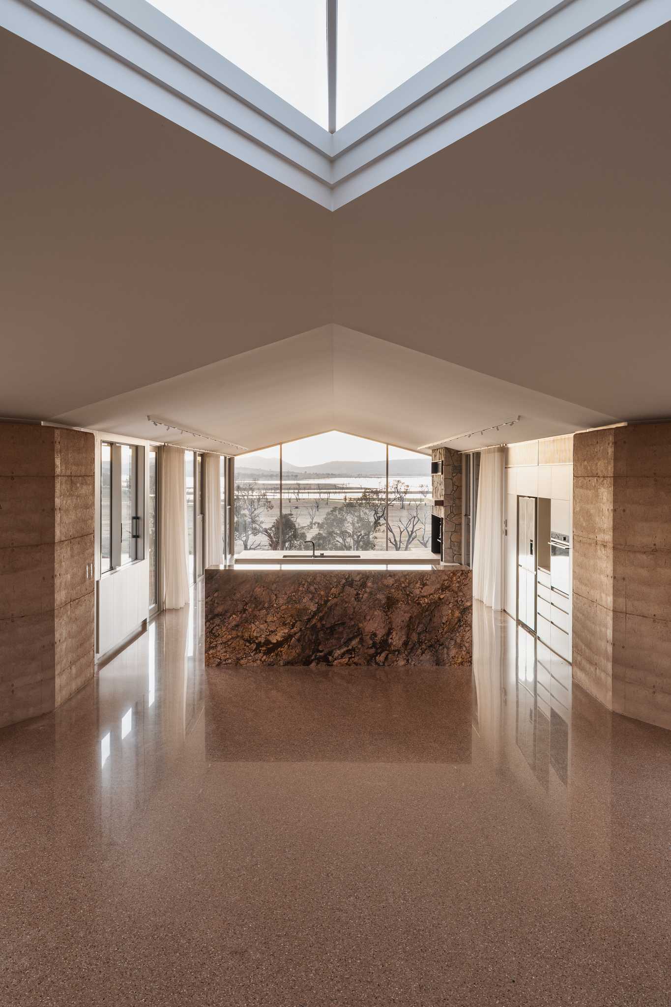 An internal frame of Table Top House in NSW. Pictured is the kitchen area with a marble island and a large window that looks out to Lake Hume.